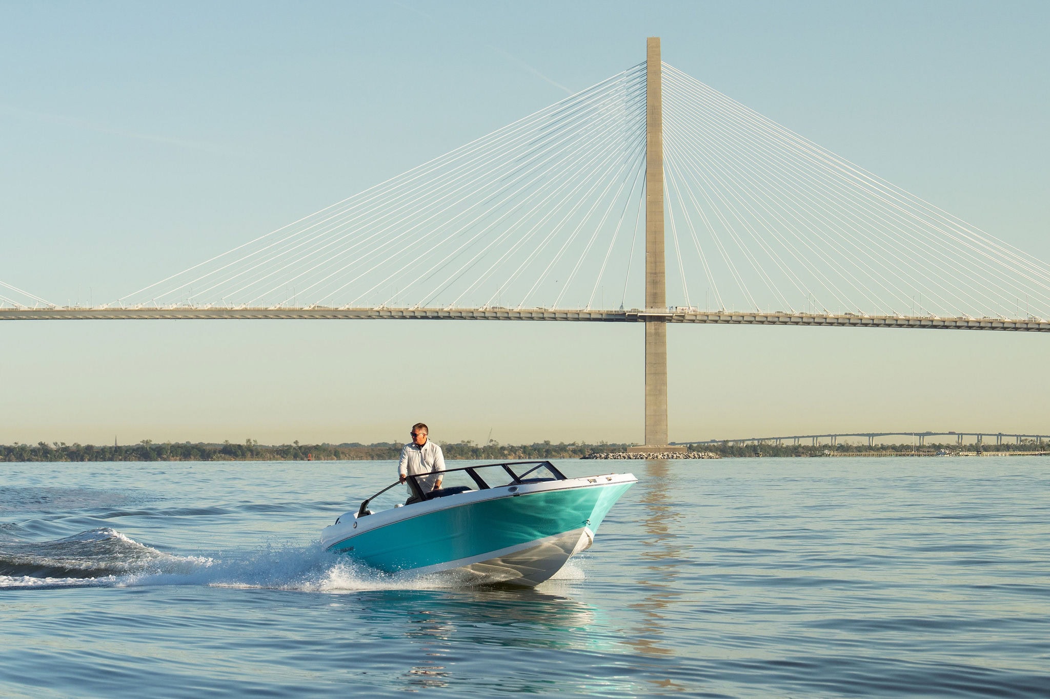Man riding a Stingray boat on water near a large cable-stayed bridge.